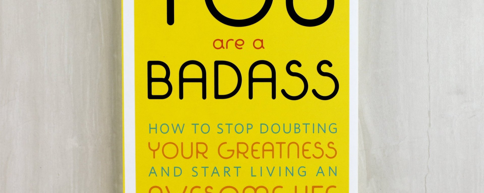 the book "you are a badass" -- a yellow book with black font. The book rests on a neutral beige background.