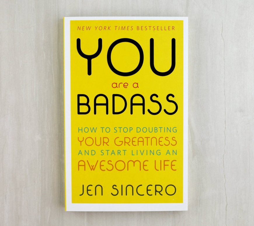 the book "you are a badass" -- a yellow book with black font. The book rests on a neutral beige background.