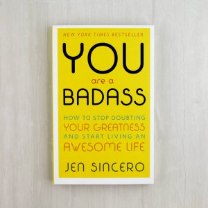 the book "you are a badass" -- a yellow book with black font. The book rests on a neutral beige background.